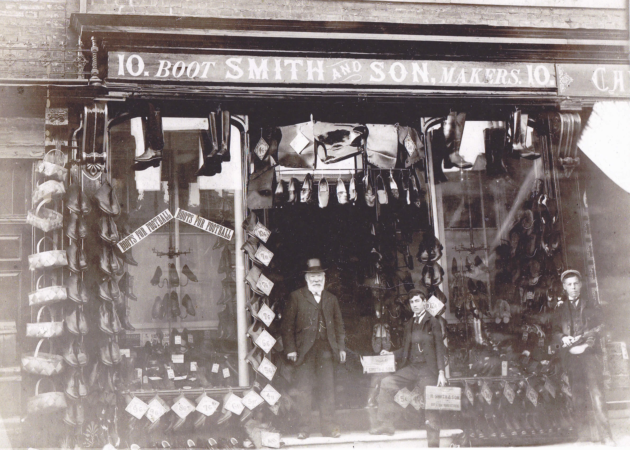 Henry Smith outside his shop filled with boots and shoes. His two young employees stand with him
