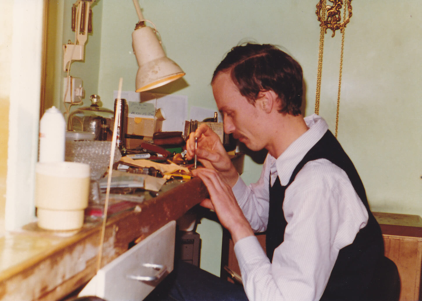 A man sits at a workbench holding small tools