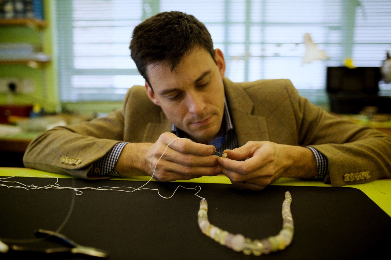 A jeweller threads beads onto silk thread.