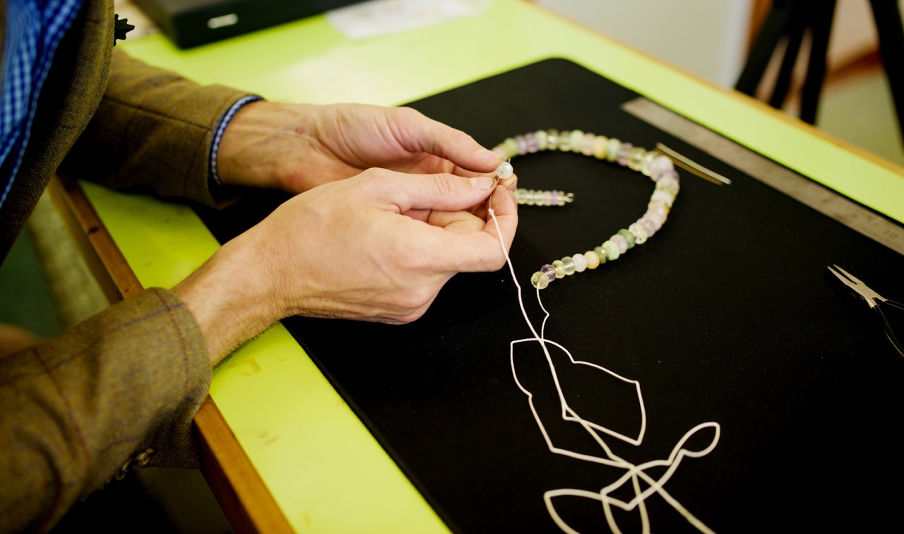 A pair of hands thread a bead onto some silk.