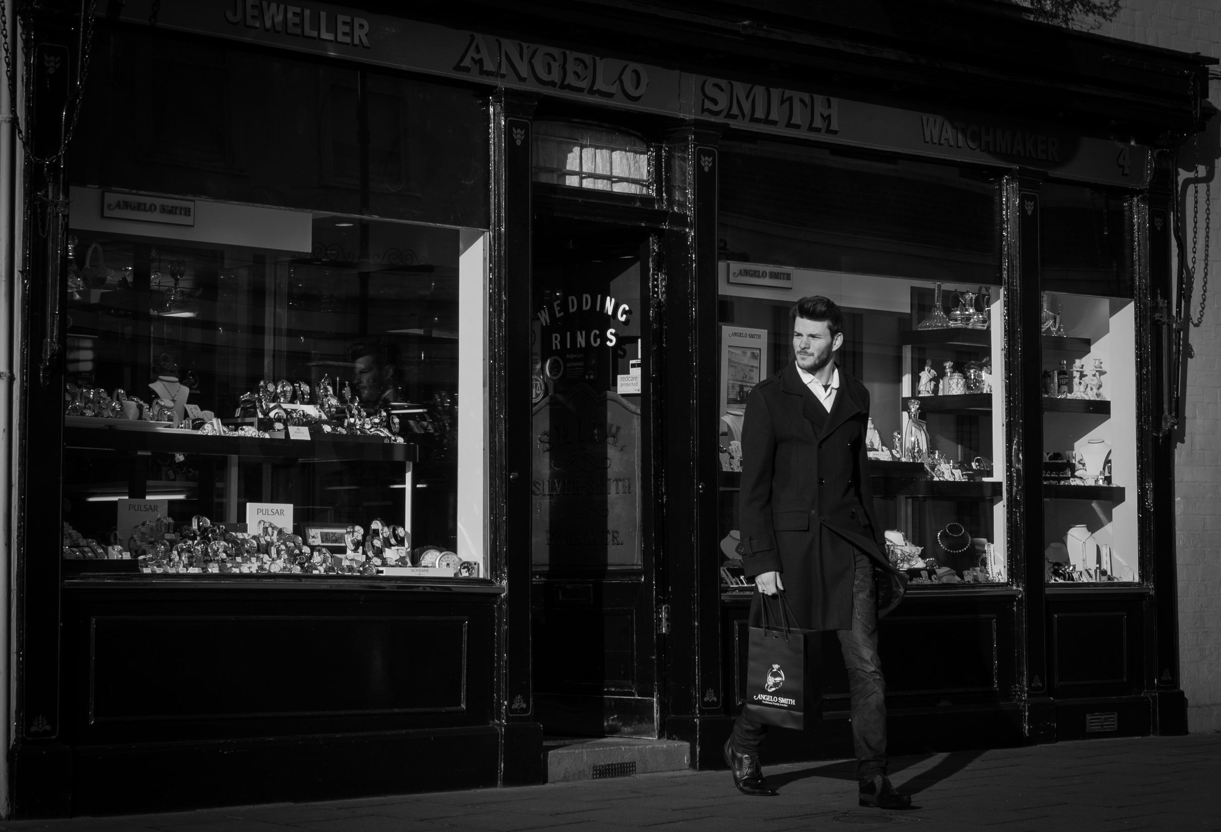 A monochrome image of a male customer leaving the showroom with an Angelo Smith branded bag in his hand.
